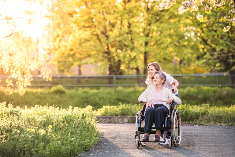 badante convivente vitto e alloggio accompagna un'anziana su sedia a rotelle in un parco