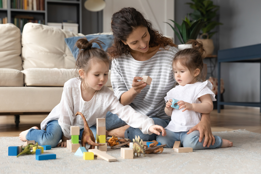 fare la babysitter: una giovane babysitter che gioca alle costruzioni con due bambine