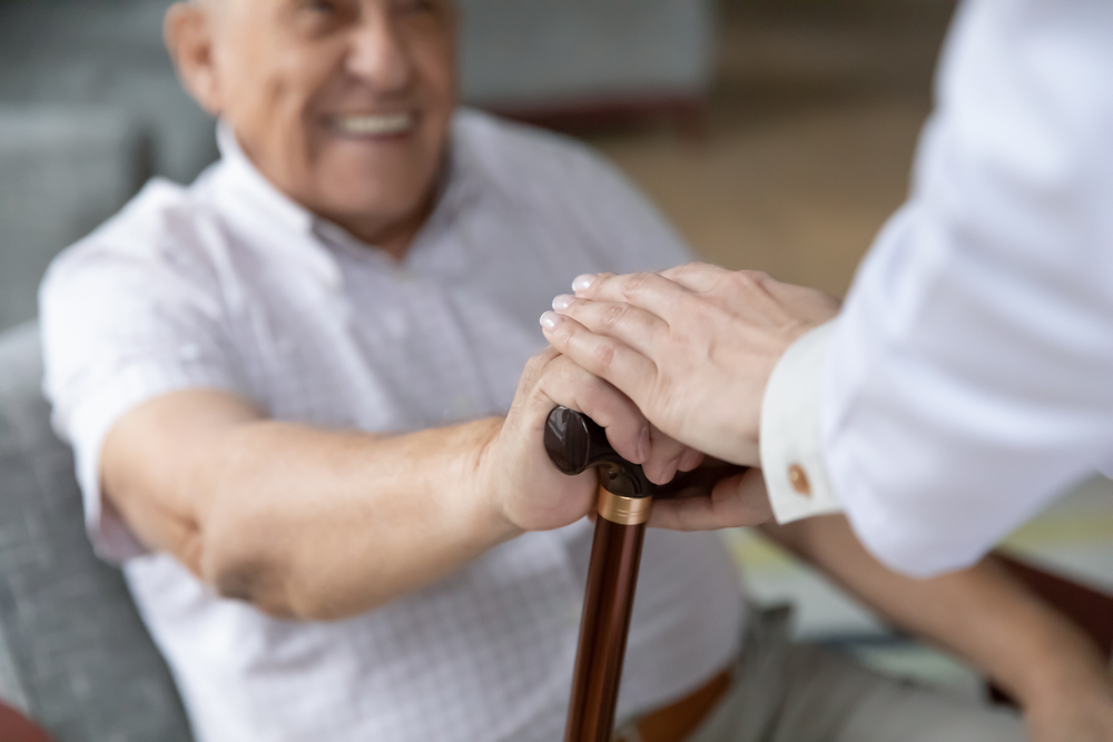 assegni di cura: anziano aiutato ad alzarsi da una badante