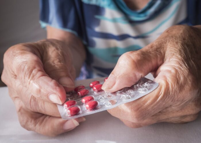 mani di anziano che aprono una confezione di pillole