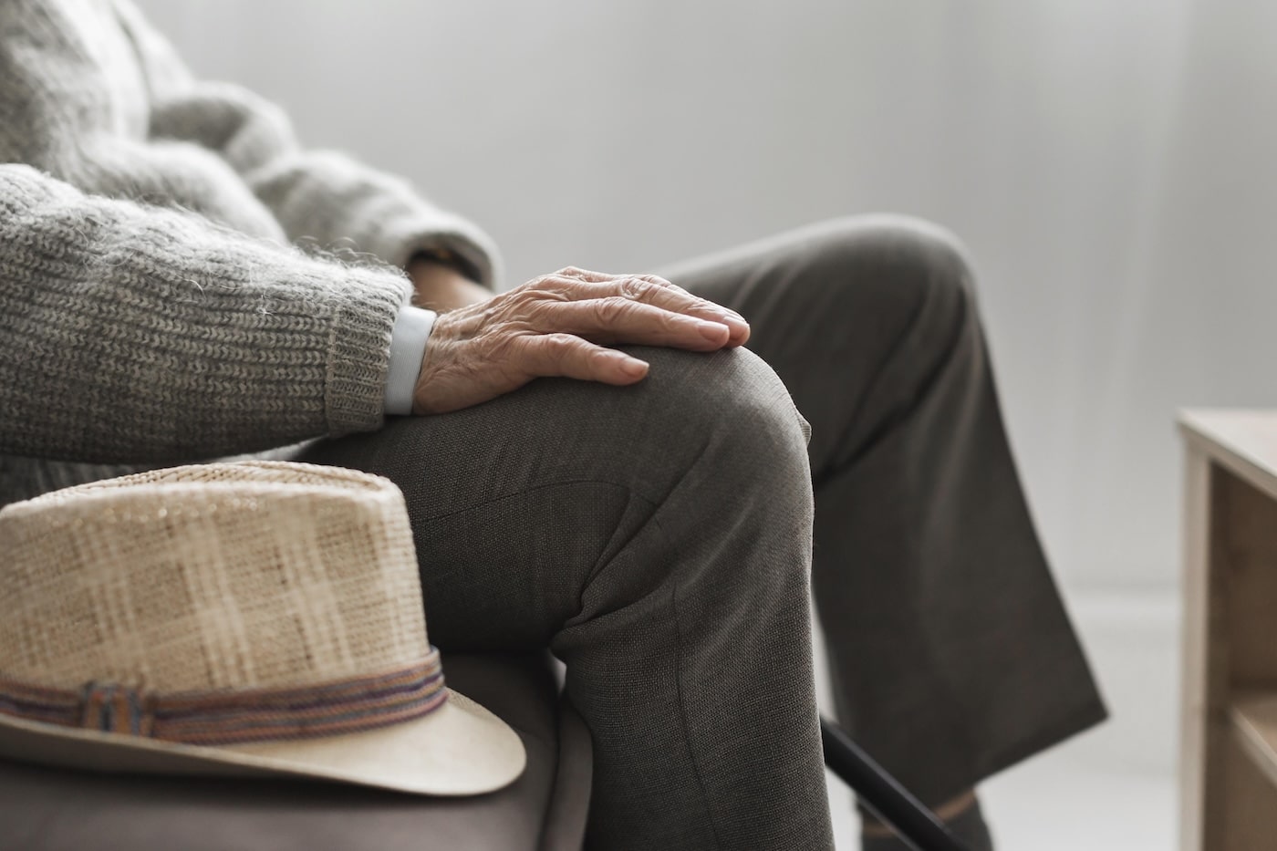 badante vitto e alloggio: persona anziana seduta con primo piano sul cappello poggiato sul tavolino e mano sul ginocchio